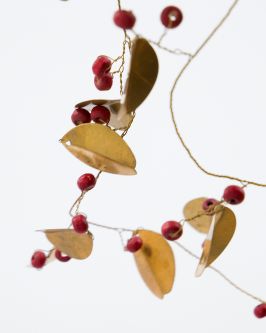 Brass coloured metal and red wooden bead garland, with a white background.