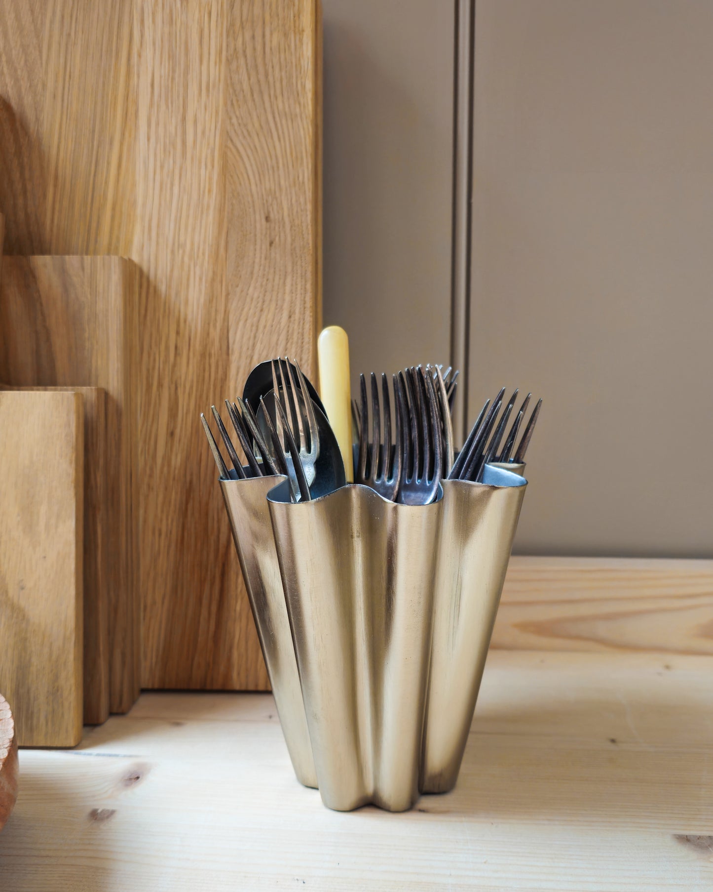 Close up of House Doctor Flood small brushed silver vase holding vintage cutlery with oak chopping boards stacked in the background.