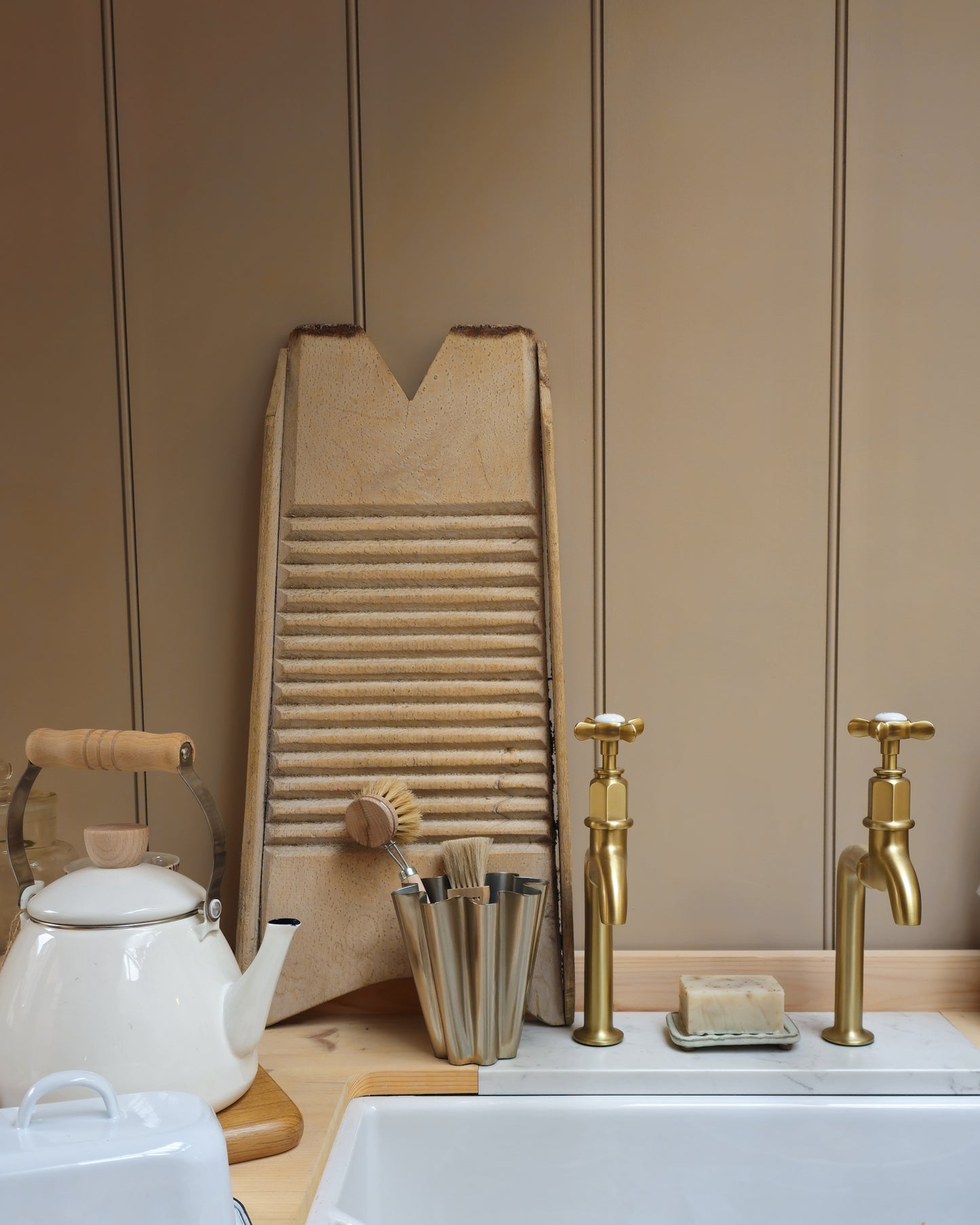 House Doctor Flood small brushed silver vase holding natural dish brushes beside a Belfast sink, vintage washboard and brass tap, and enamel kettle and butterdish.