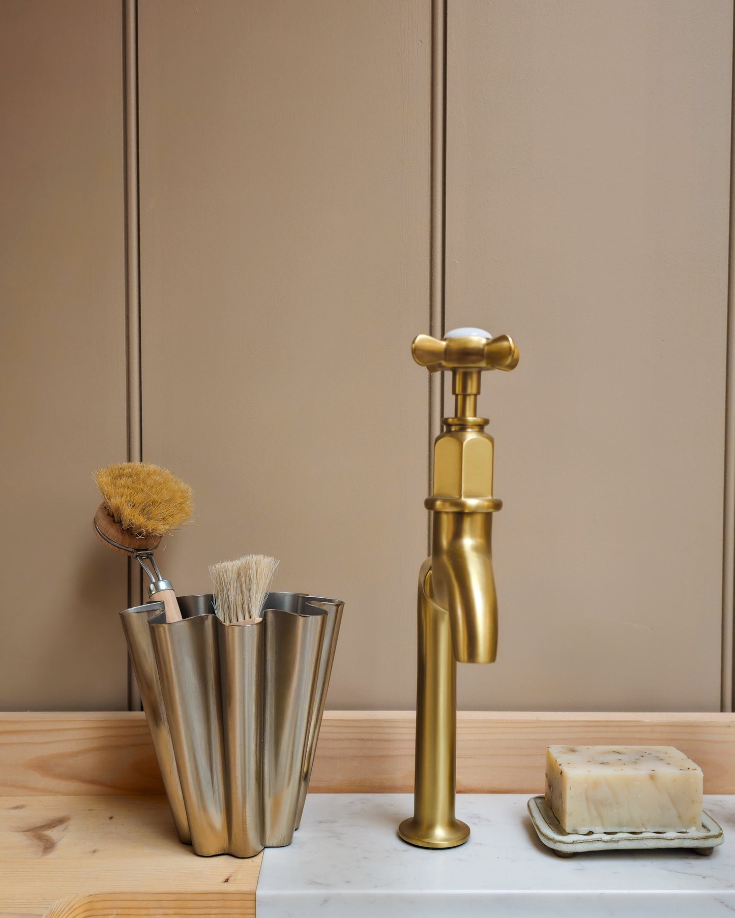 Close detail of House Doctor Flood small brushed silver vase with natural dish brushes beside a brass tap and natural soap.