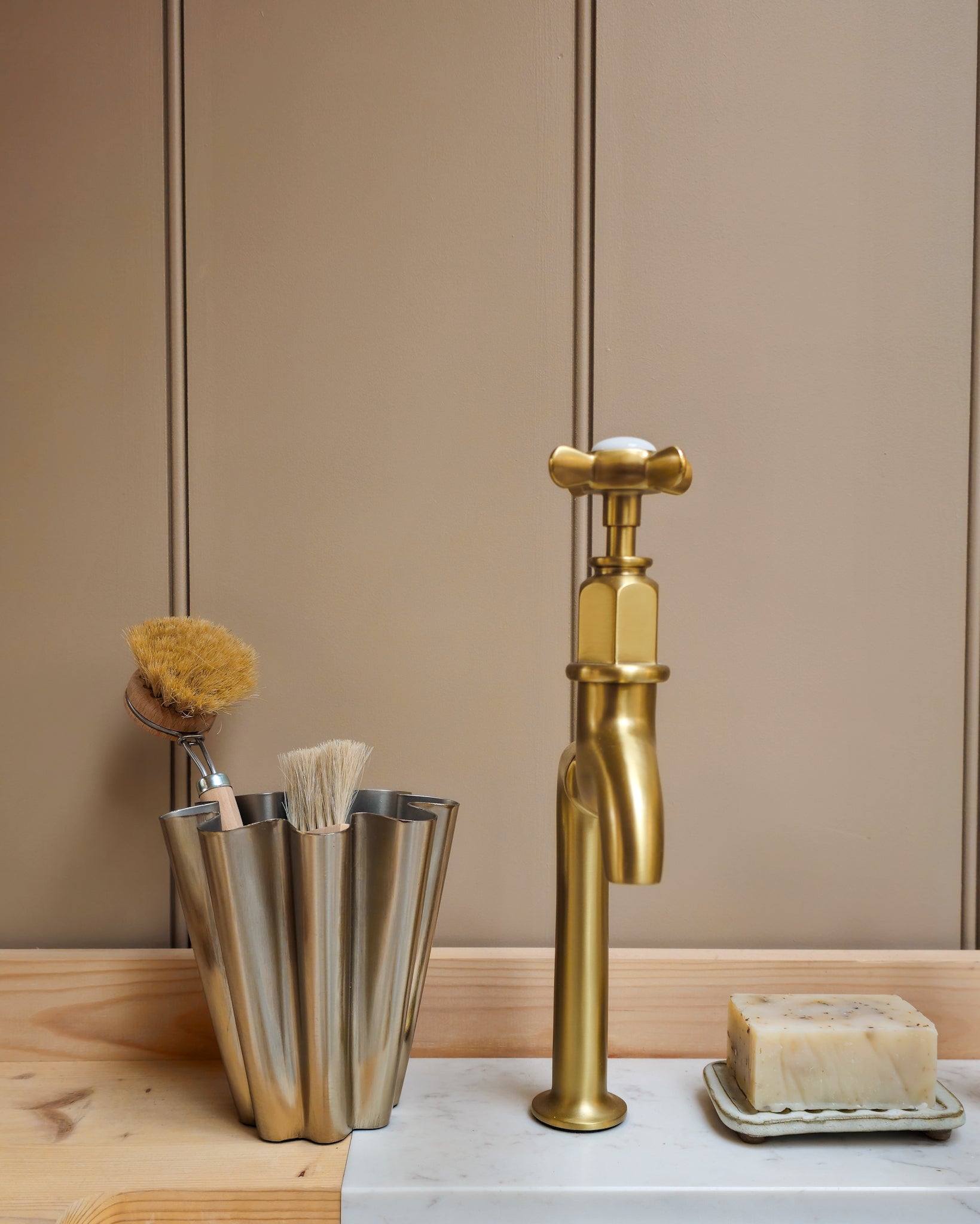 Close detail of House Doctor Flood small brushed silver vase with natural dish brushes beside a brass tap and natural soap.