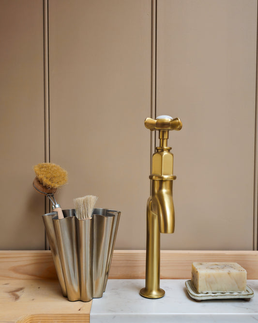 Close detail of House Doctor Flood small brushed silver vase with natural dish brushes beside a brass tap and natural soap.