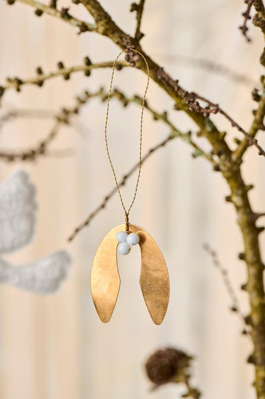 Decorative brass leaf ornament hanging from a branch with a blurred background
