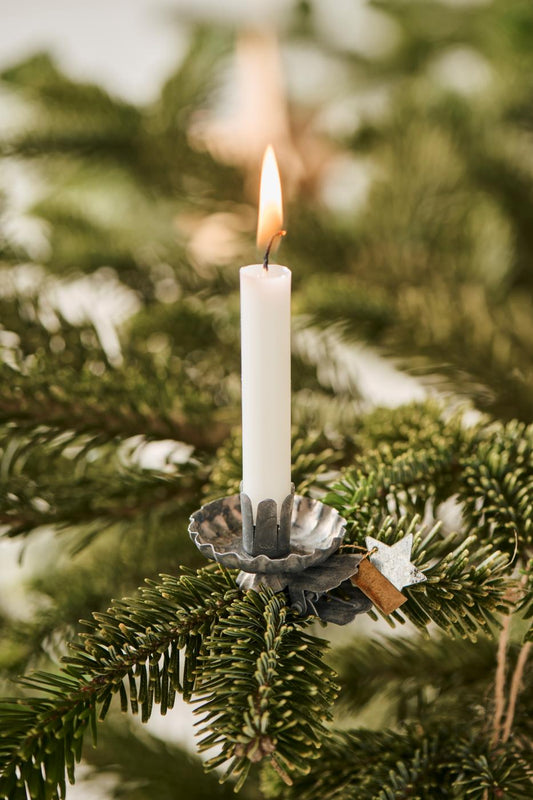 White candle in a decorative holder on a Christmas tree branch