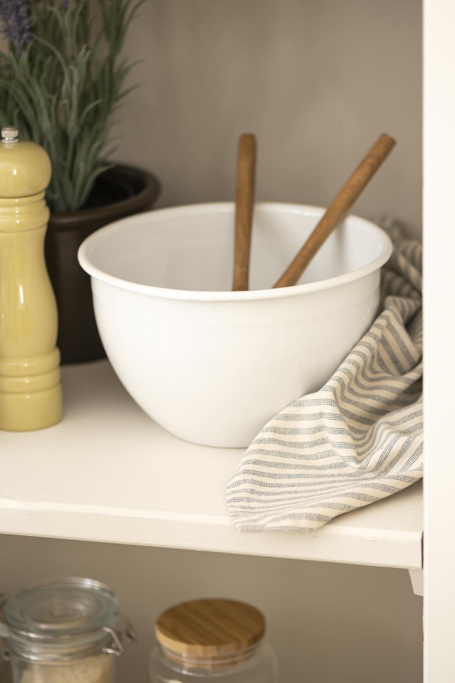 White mixing bowl with wooden spoons on a shelf with jars and a plant in the background