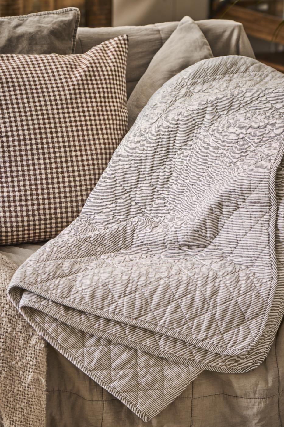 A vintage style grey striped quilt laid over a sofa, surrounded by cushions.