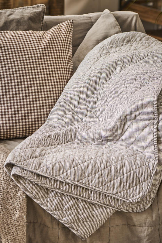 A vintage style grey striped quilt laid over a sofa, surrounded by cushions.