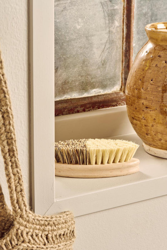 Bristle brush on a wooden stand next to a textured vase in a bathroom setting.