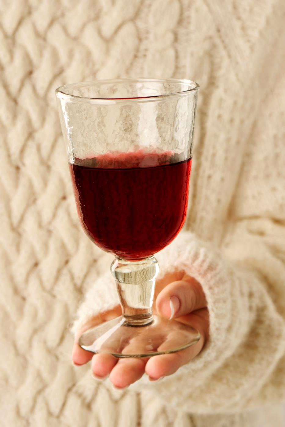 Hand holding a glass of red liquid against a textured beige background