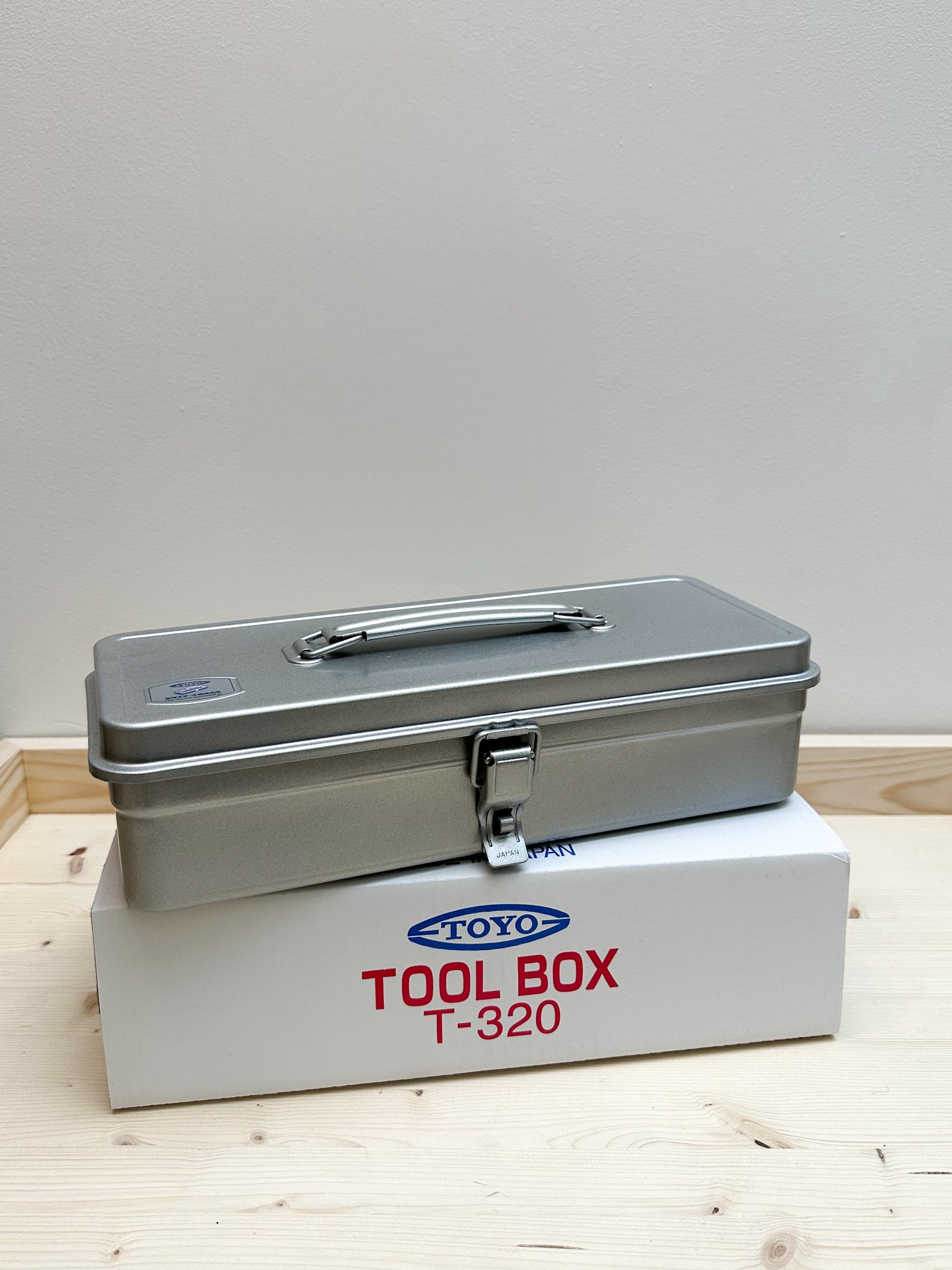 A silver metal tool box with a lid, placed on a wooden surface, with the branding 'TOYO TOOL BOX T-320' visible on the front.