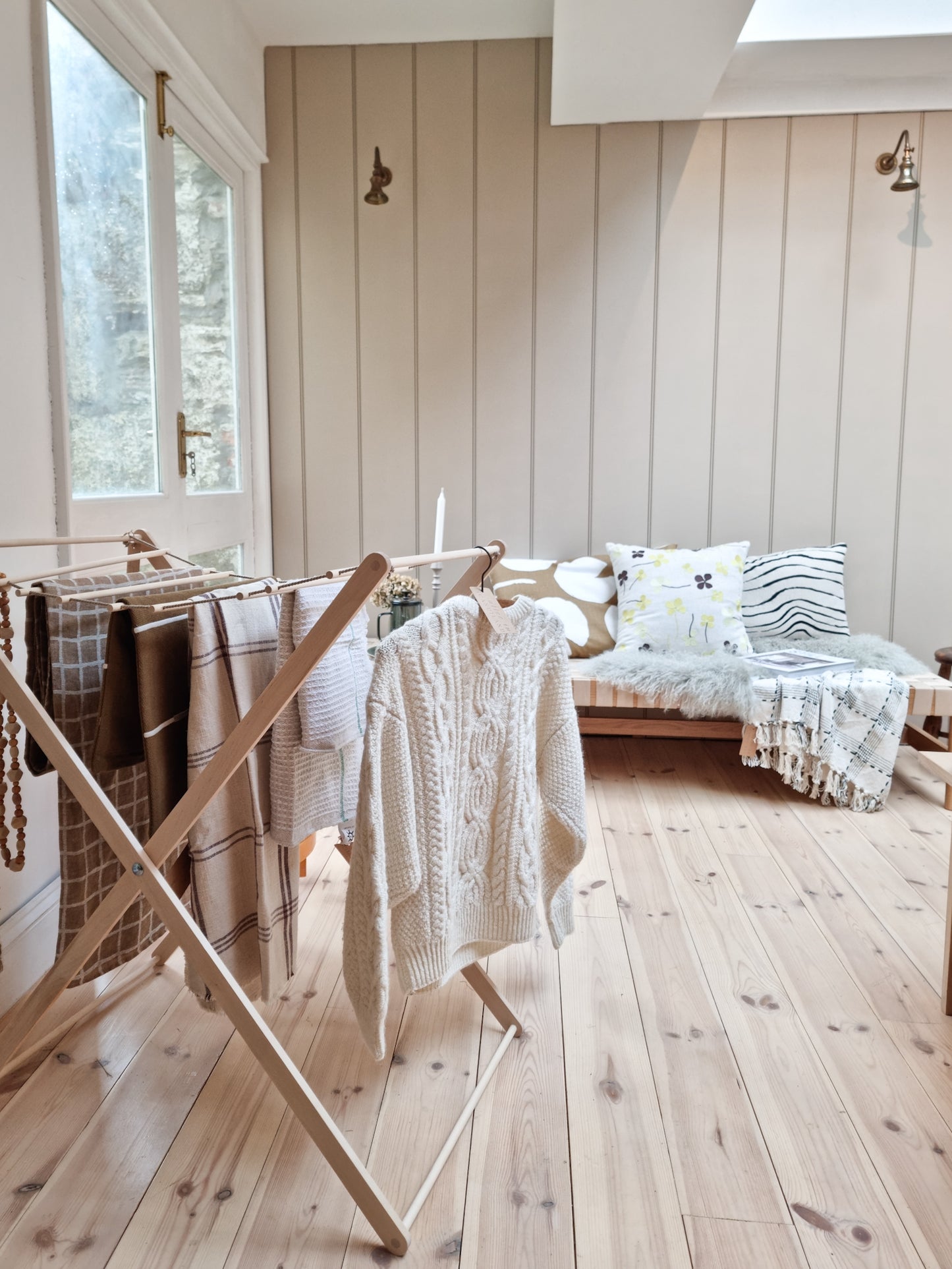 Foldable wooden wash drier airer with clothes drying on it, placed in a light filled room with a wooden floor.