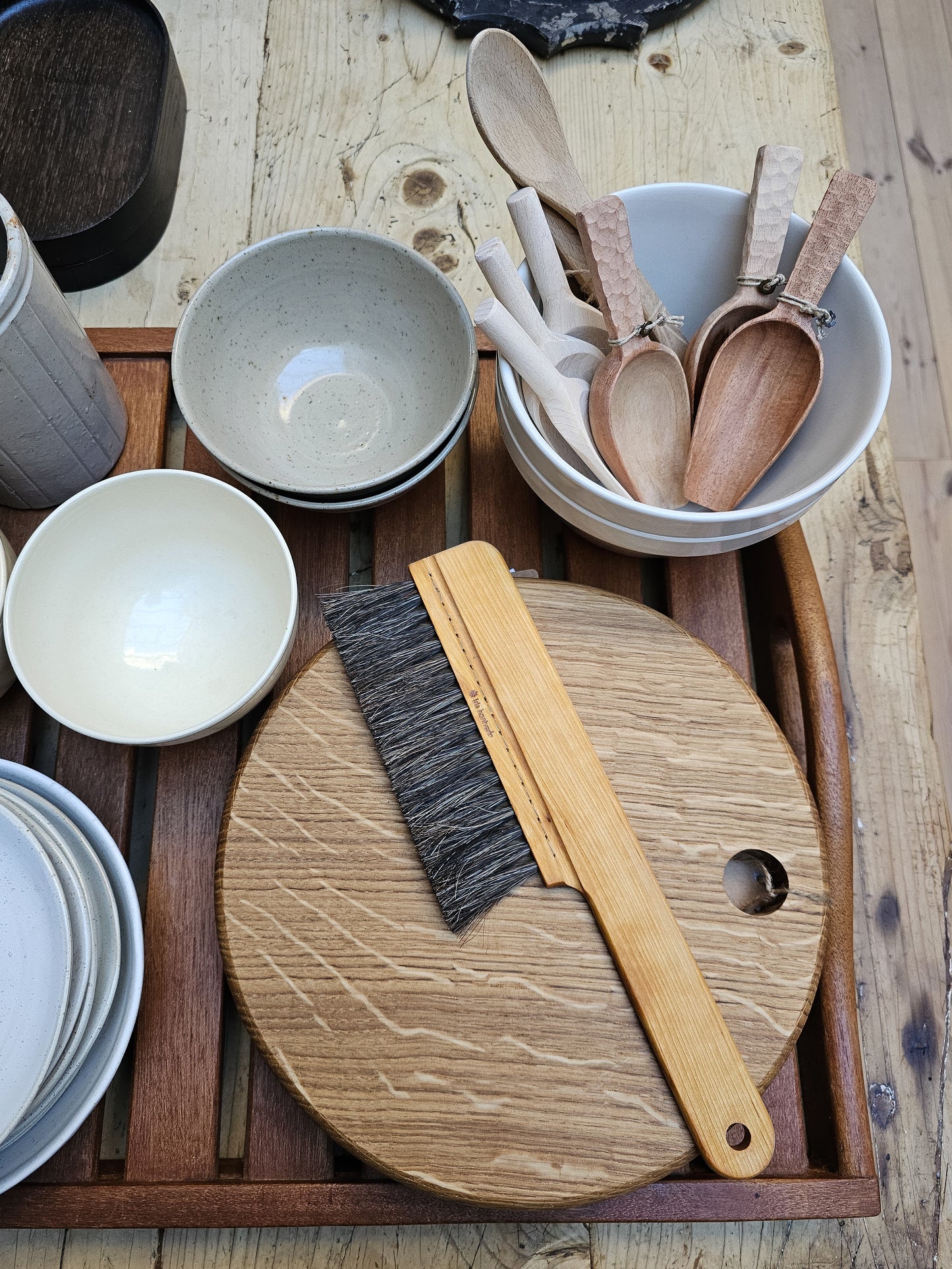 A wooden table brush with a handle, displayed on a table alongside other kitchen utensils and dishes.