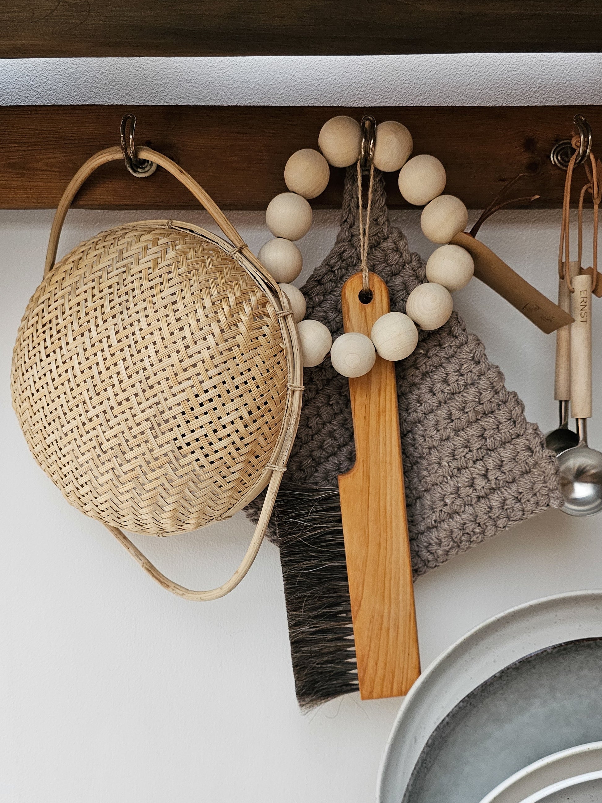 A wooden table brush hanging on a peg rail with various other kitchen appliances.