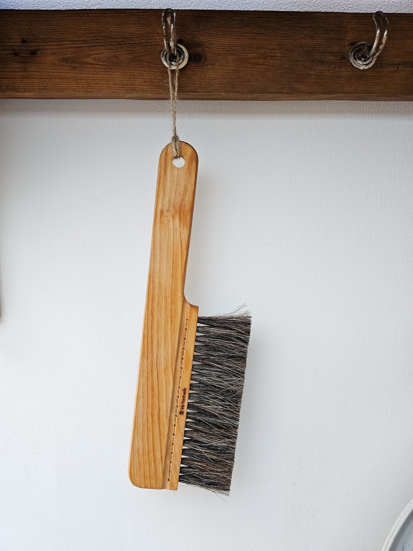 A wooden table brush hanging on a wooden peg rail against a white background.