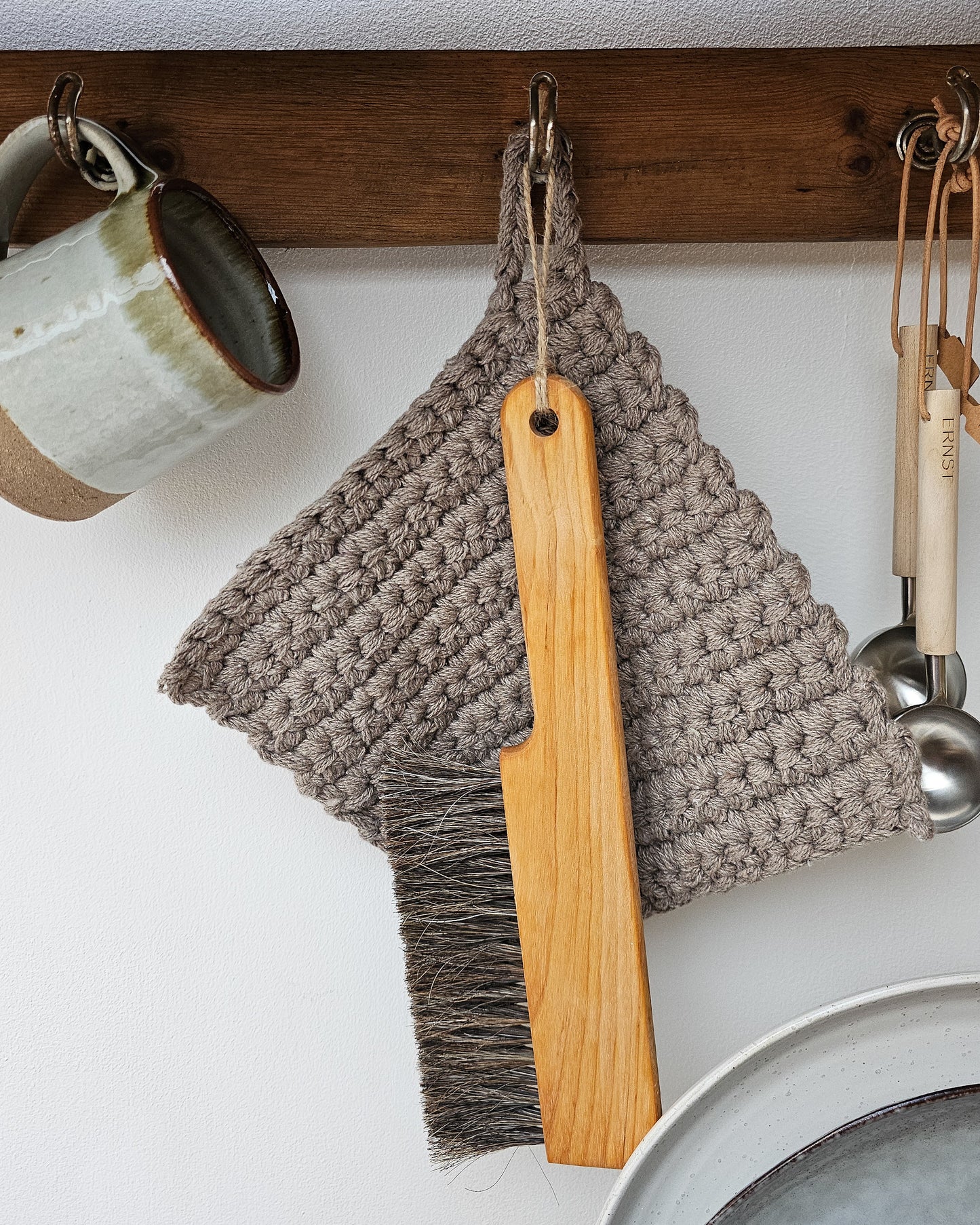 A wooden table brush hanging on a peg rail with various other kitchen appliances.