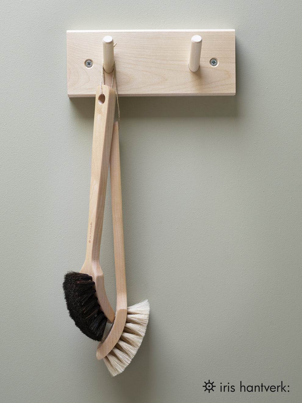 A peg rail rack made of birch wood with multiple hooks, mounted on a wall and holding a couple of brushes.