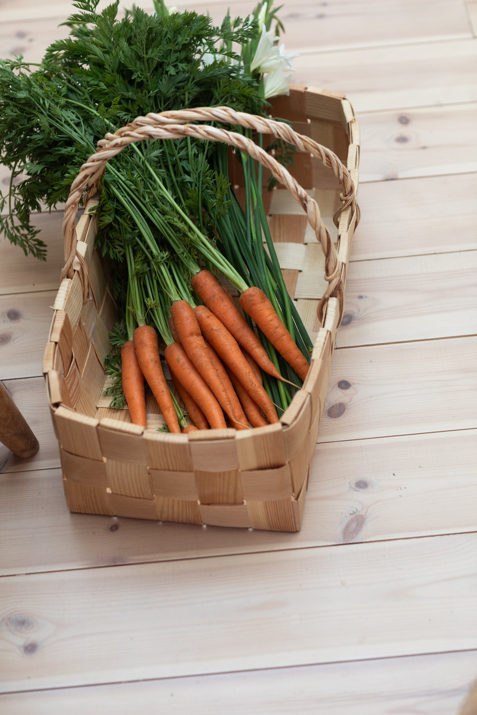 A pine woven basket filled with fresh carrots on a wooden surface.
