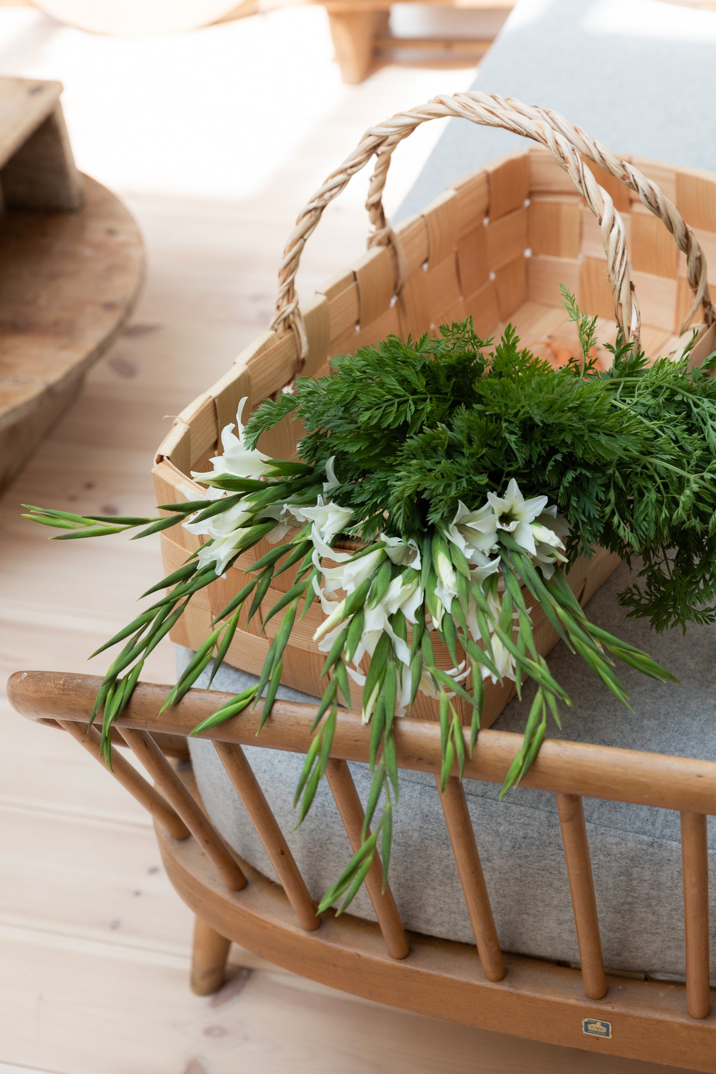 Woven basket full of flowers placed on a sofa/bench.