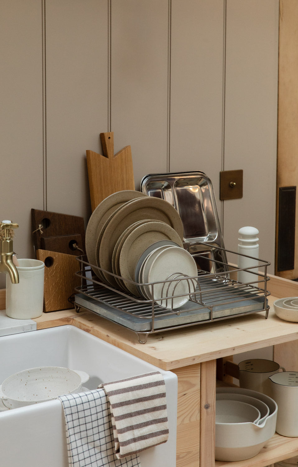 Silver iron dish rack full of stoneware plates beside a butler sink with chopping boards behind