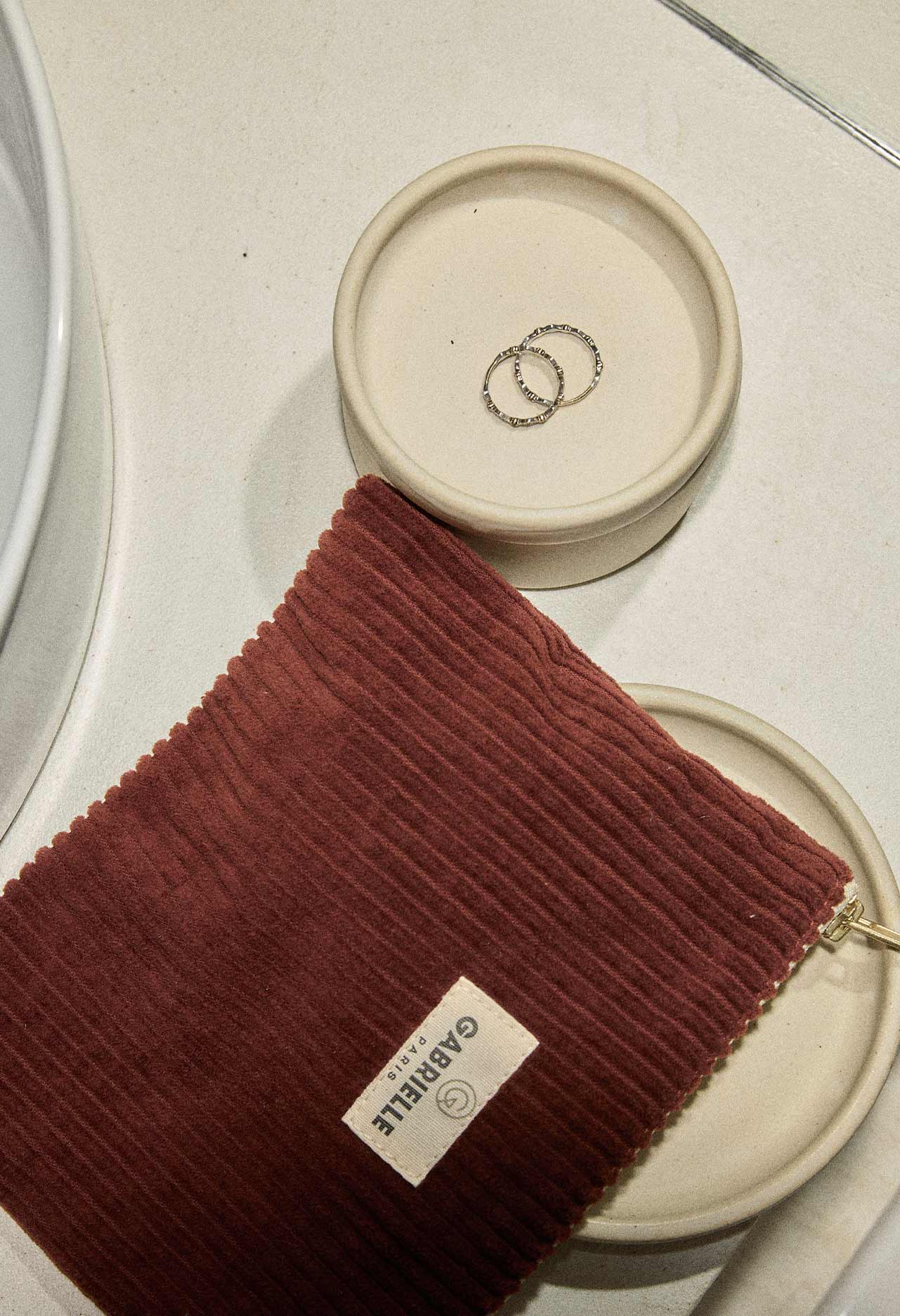 Red wine coloured velvet pouch with a Gabrielle Paris label sat on top of a beige dish containing rings.