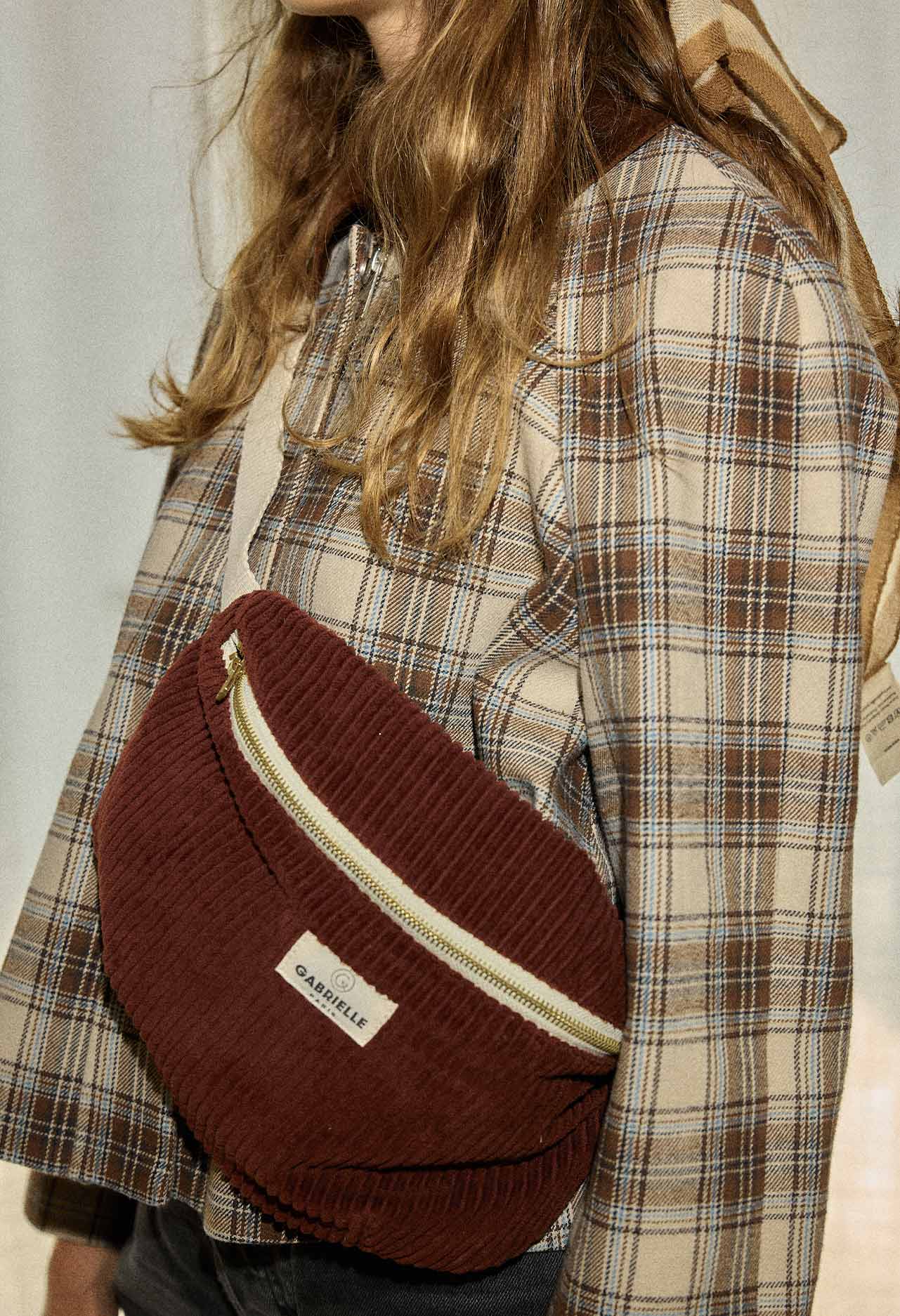 Person wearing a red-wine corduroy bag cross body over a plaid shirt.