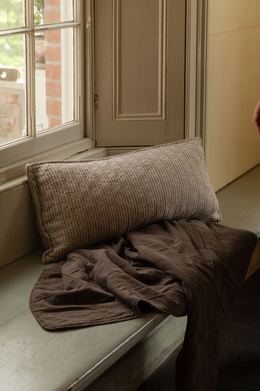Kantha stitch striped cushion in natural and brown on a window seat, with a soft brown stonewashed quilt