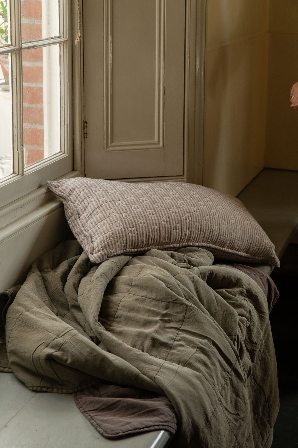 Kantha stitch striped cushion on a crumpled eucalyptus green stonewashed quilt in a window seat