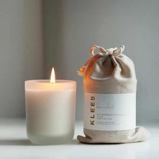 Kleensoaps Blue Velvet coconut wax candle lit beside its cotton drawstring bag, scented with bergamot, patchouli and clove