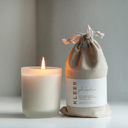 Kleensoaps Good Vibrations coconut wax candle lit beside its cotton drawstring bag, scented with lemongrass, rosemary and grapefruit