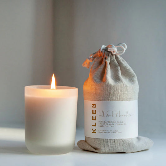 Kleensoaps Tall Dark and Handsome coconut wax candle lit beside its cotton drawstring bag, scented with patchouli, clove, sweet orange and cinnamon