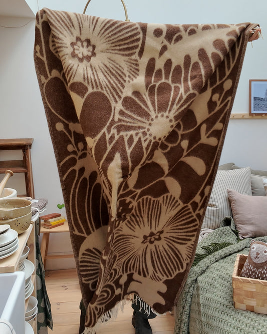 Alice holds up a brown and cream graphic flower patterned wool blanket.