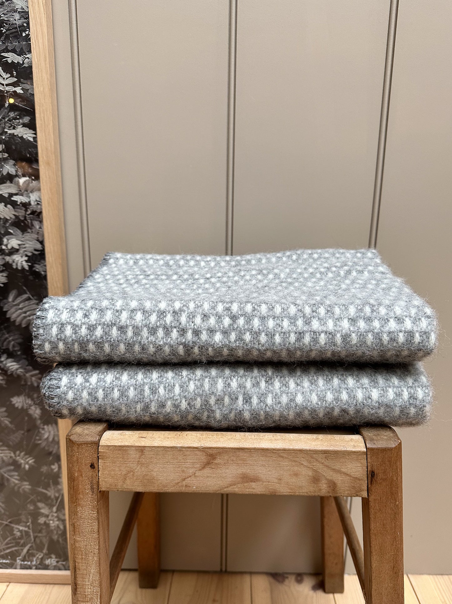 Two Klippan Knut Lambswool baby blankets folded on top of each other on a wooden stool.