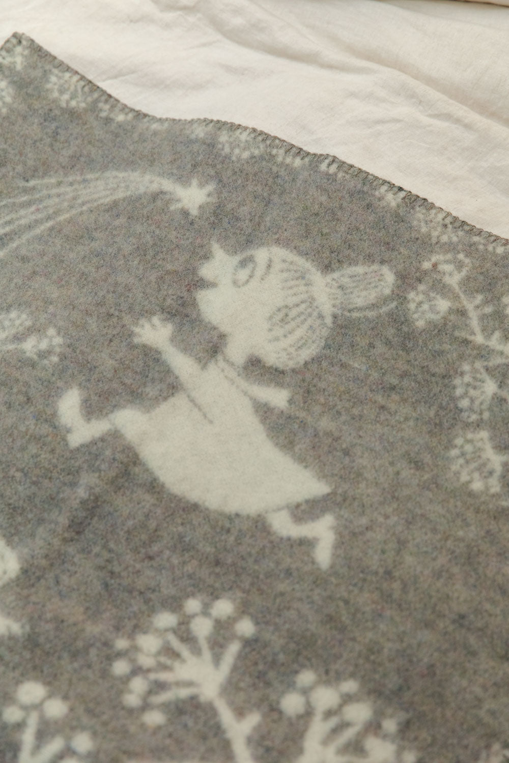 Close-up of Klippan Moomin recycled lambswool baby blanket showing Little My character on the grey reverse side with blanket stitched edge detail.