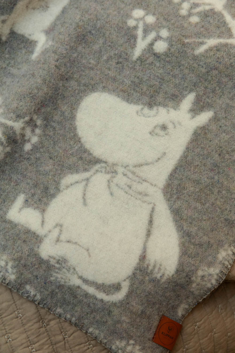 Close-up of Klippan Moomin recycled lambswool baby blanket in grey and cream showing Moomintroll character detail and Klippan leather label.