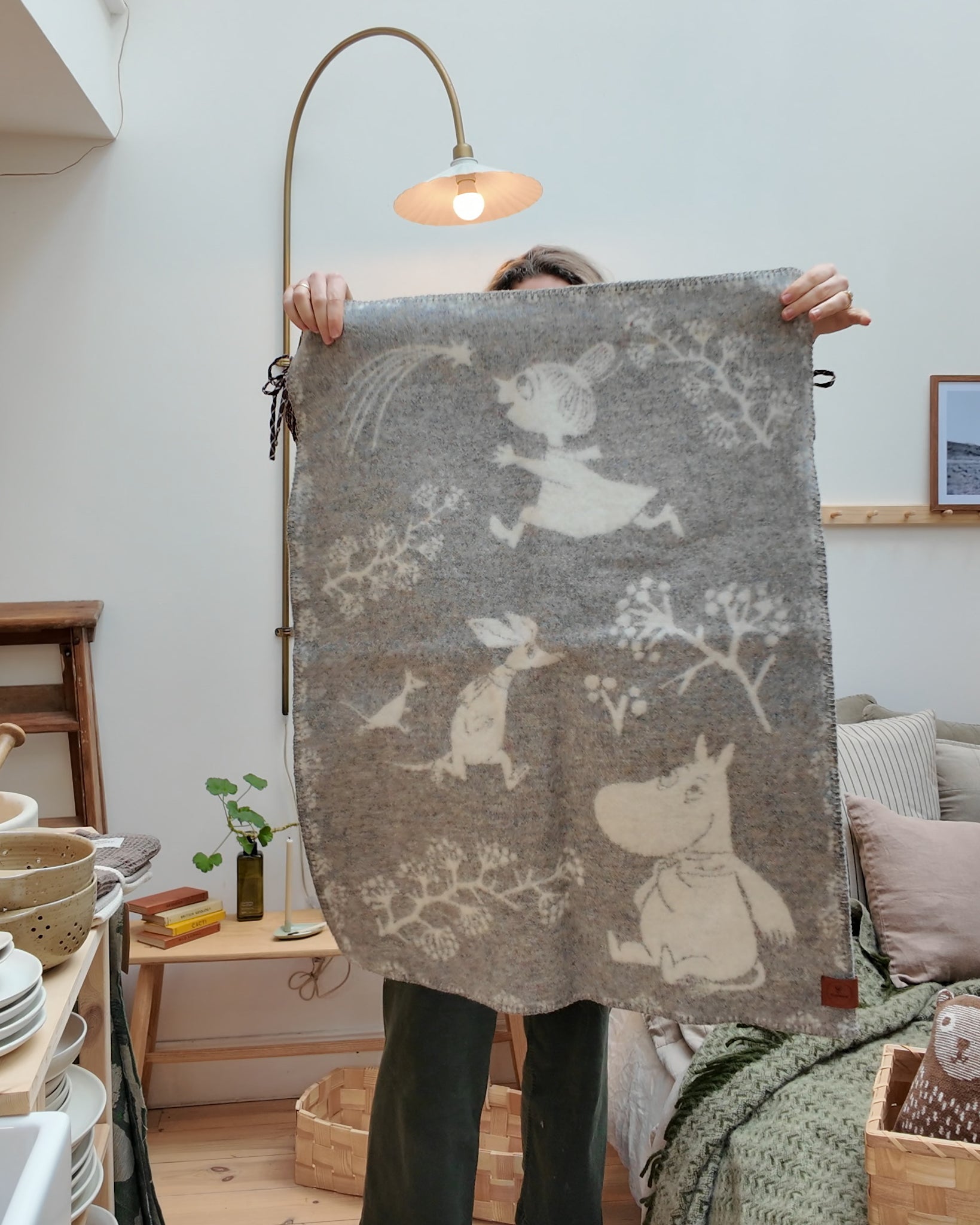 Scandinavian styled room with Alice holding up a grey and white moomin Children’s wool blanket.