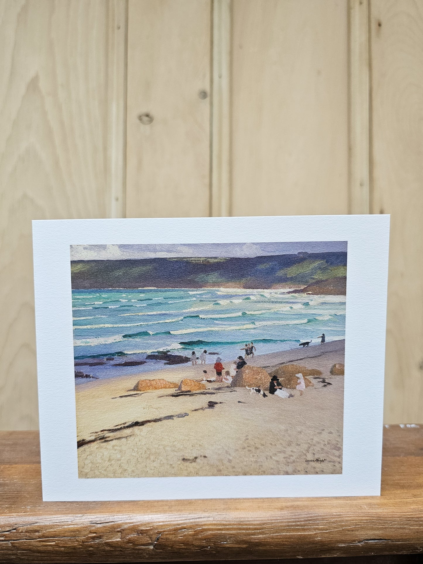 Greeting card reproducing Laura Knight's oil painting A Dark Pool, showing a solitary woman in a red dress standing on coastal rocks gazing out to a calm blue sea