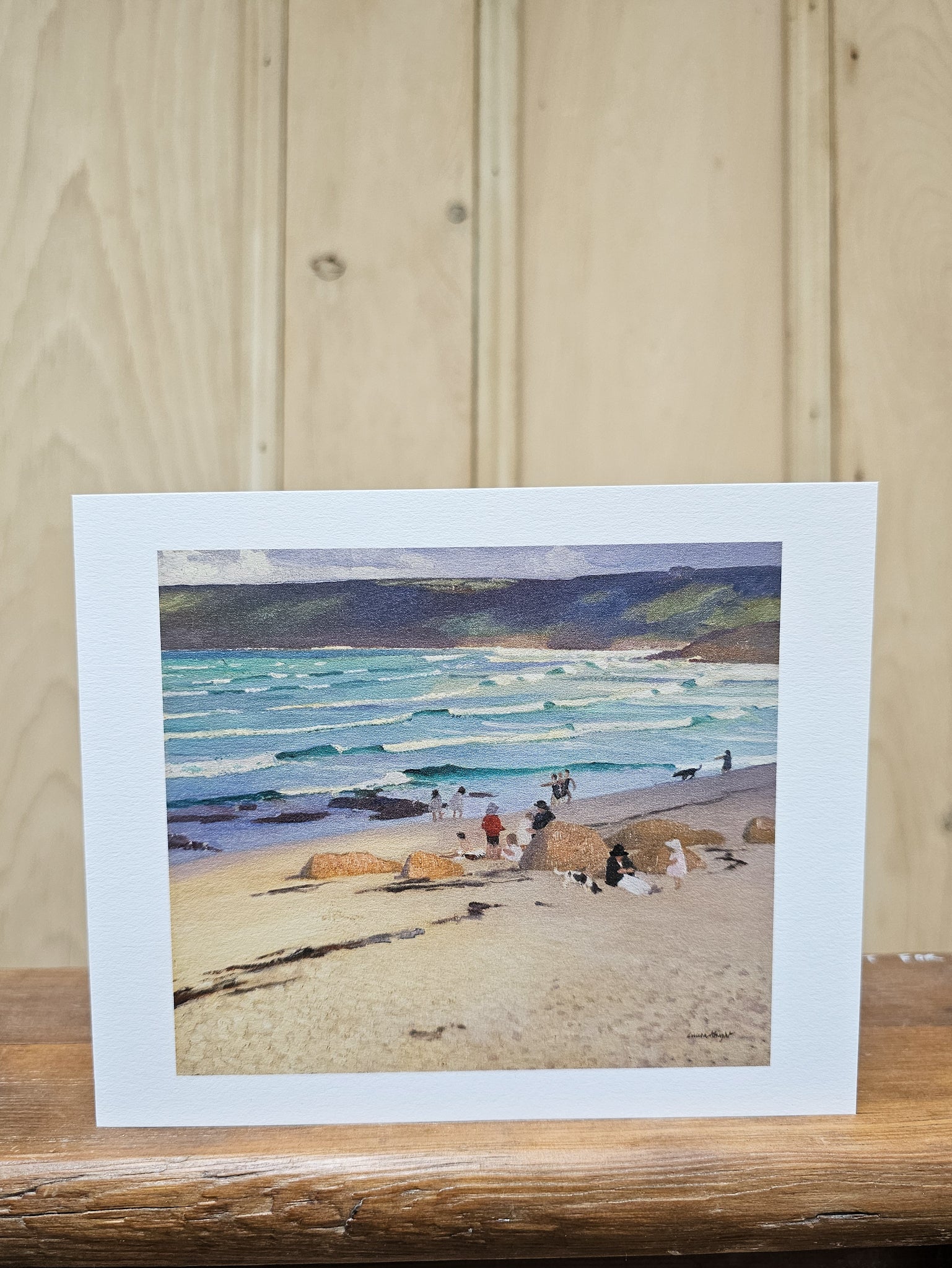 Greeting card reproducing Laura Knight's oil painting A Dark Pool, showing a solitary woman in a red dress standing on coastal rocks gazing out to a calm blue sea