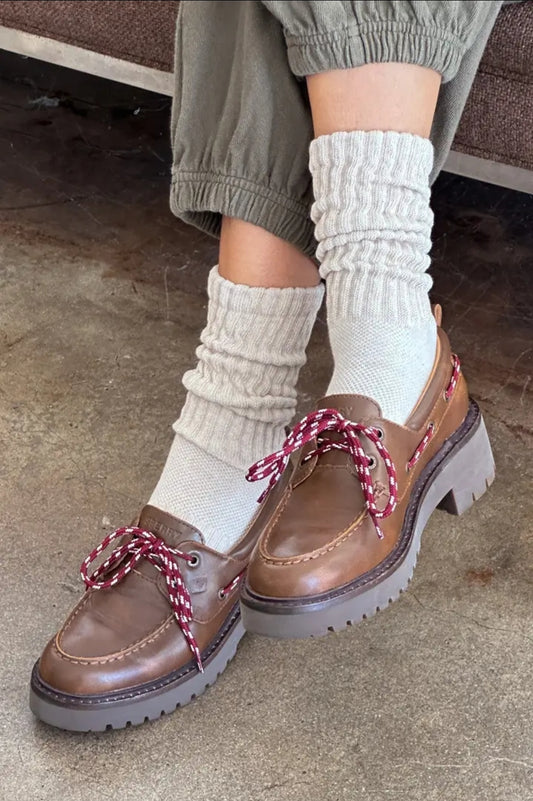Brown shoes with red laces worn with oatmeal socks on a concrete floor.