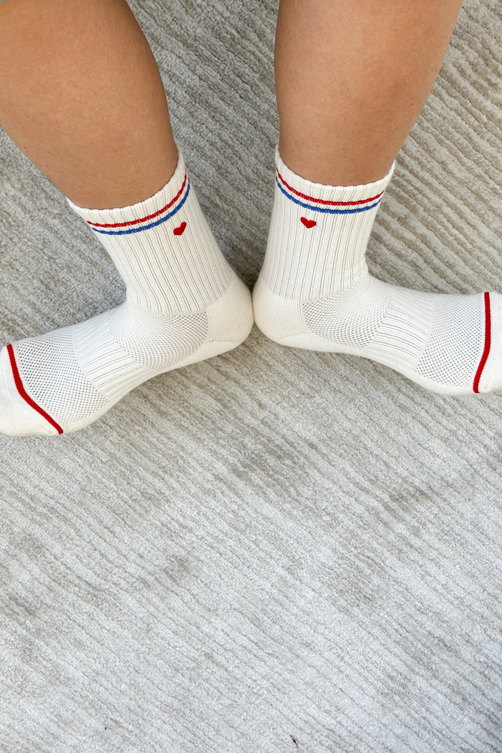 Two feet on a grey background wearing Le Bon Shoppe Boyfriend Sock in the embroidered white/blue/red colourway.