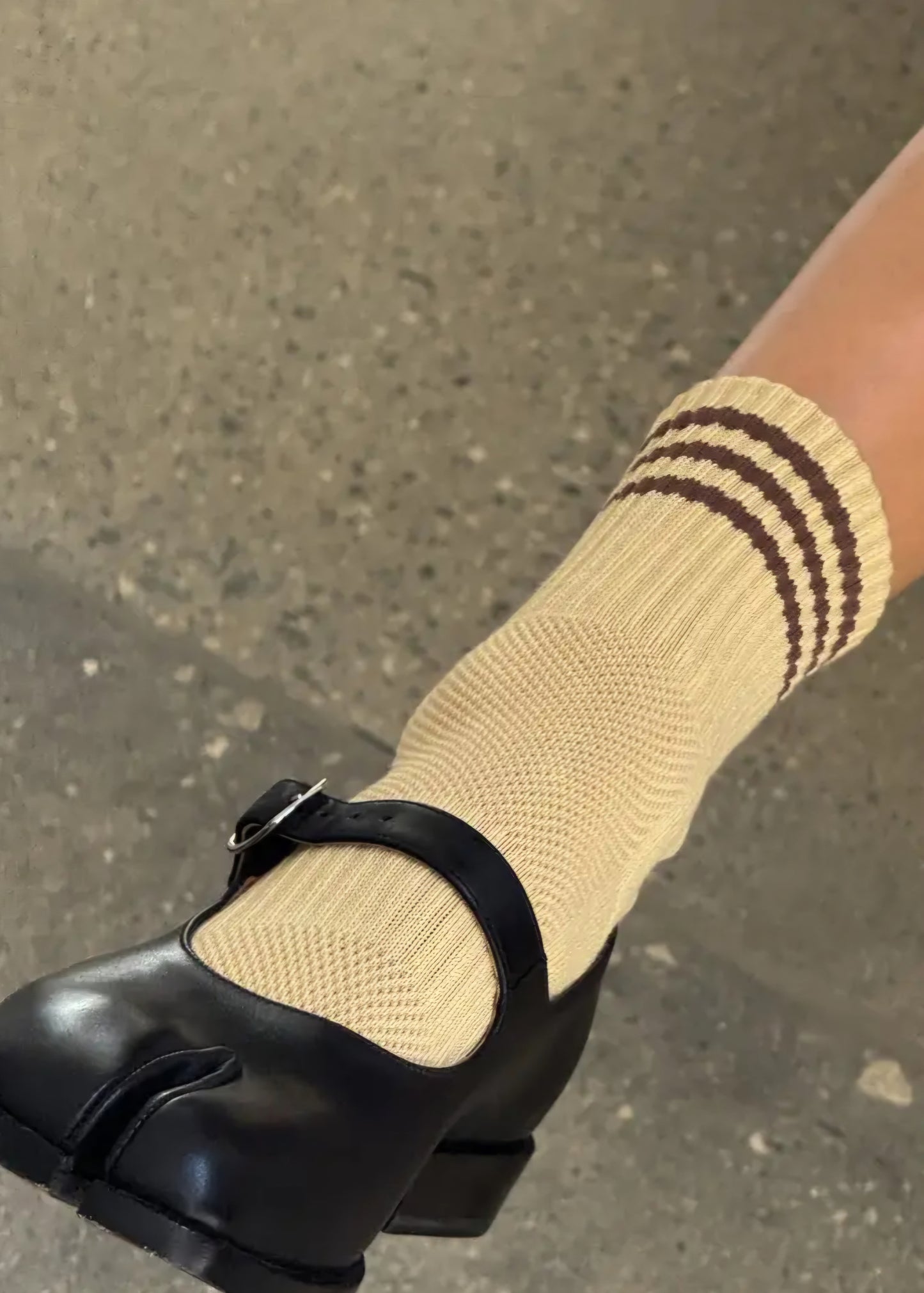 Light yellow sock with brown stripes worn with a black shoe on a concrete surface.