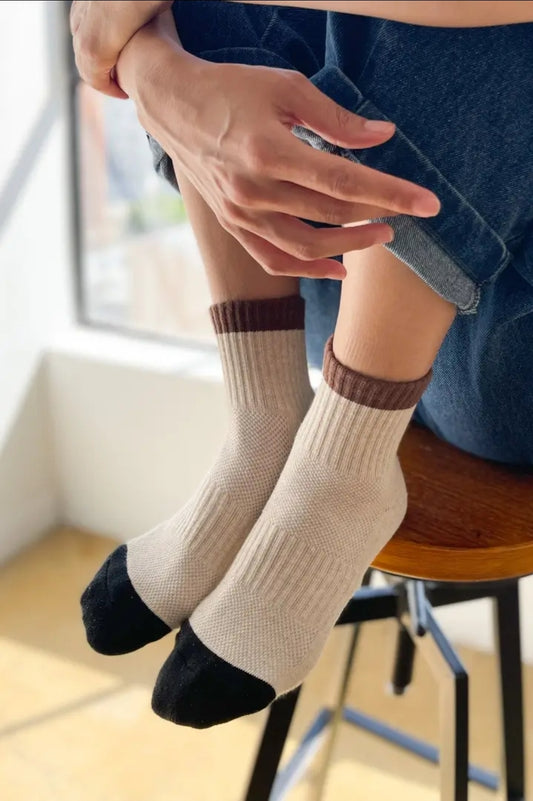 Person wearing beige socks with brown and black accents sitting on a chair.