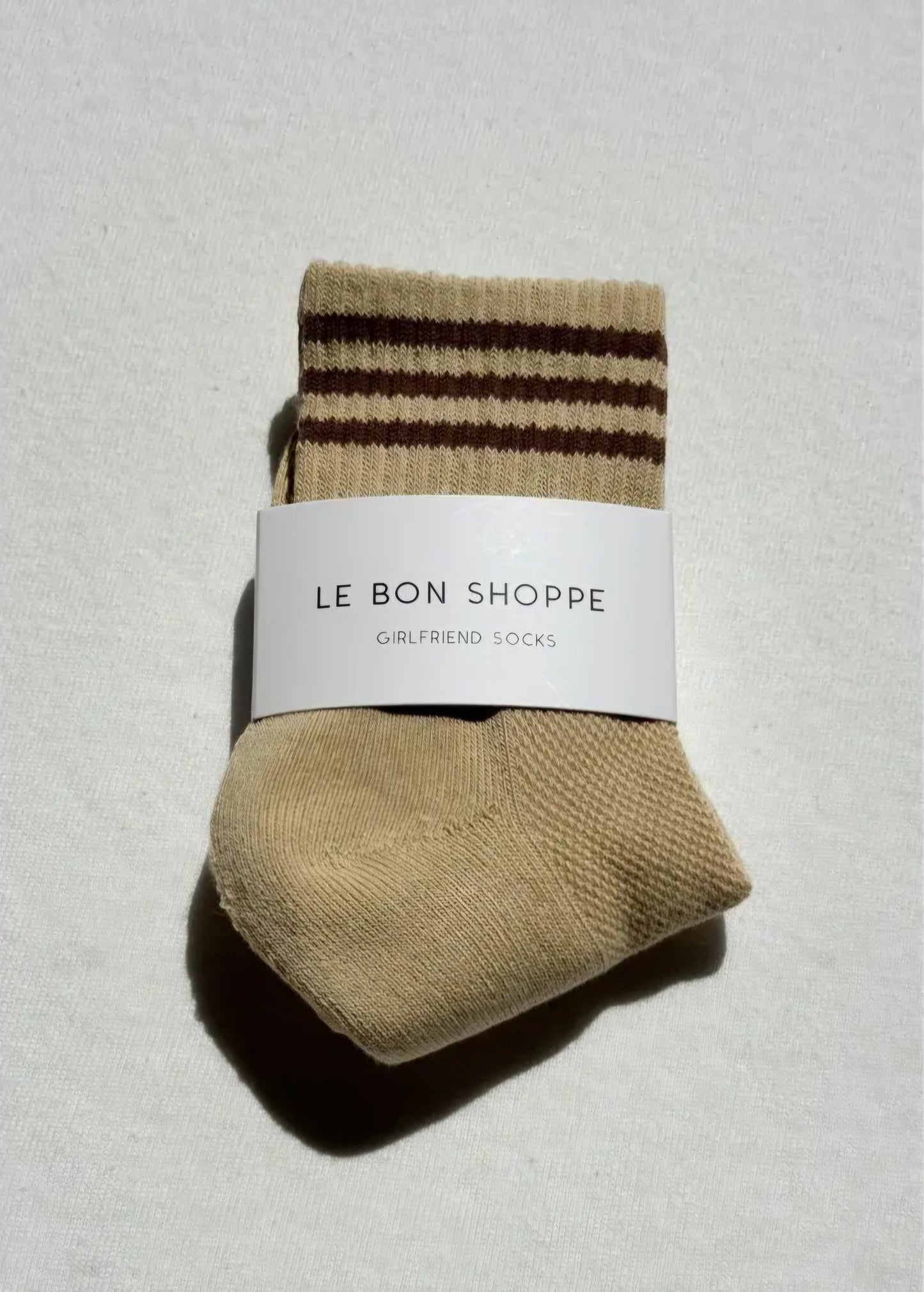 Pair of light yellow socks with brown stripes on a light grey background, featuring 'Le Bon Shoppe' label.