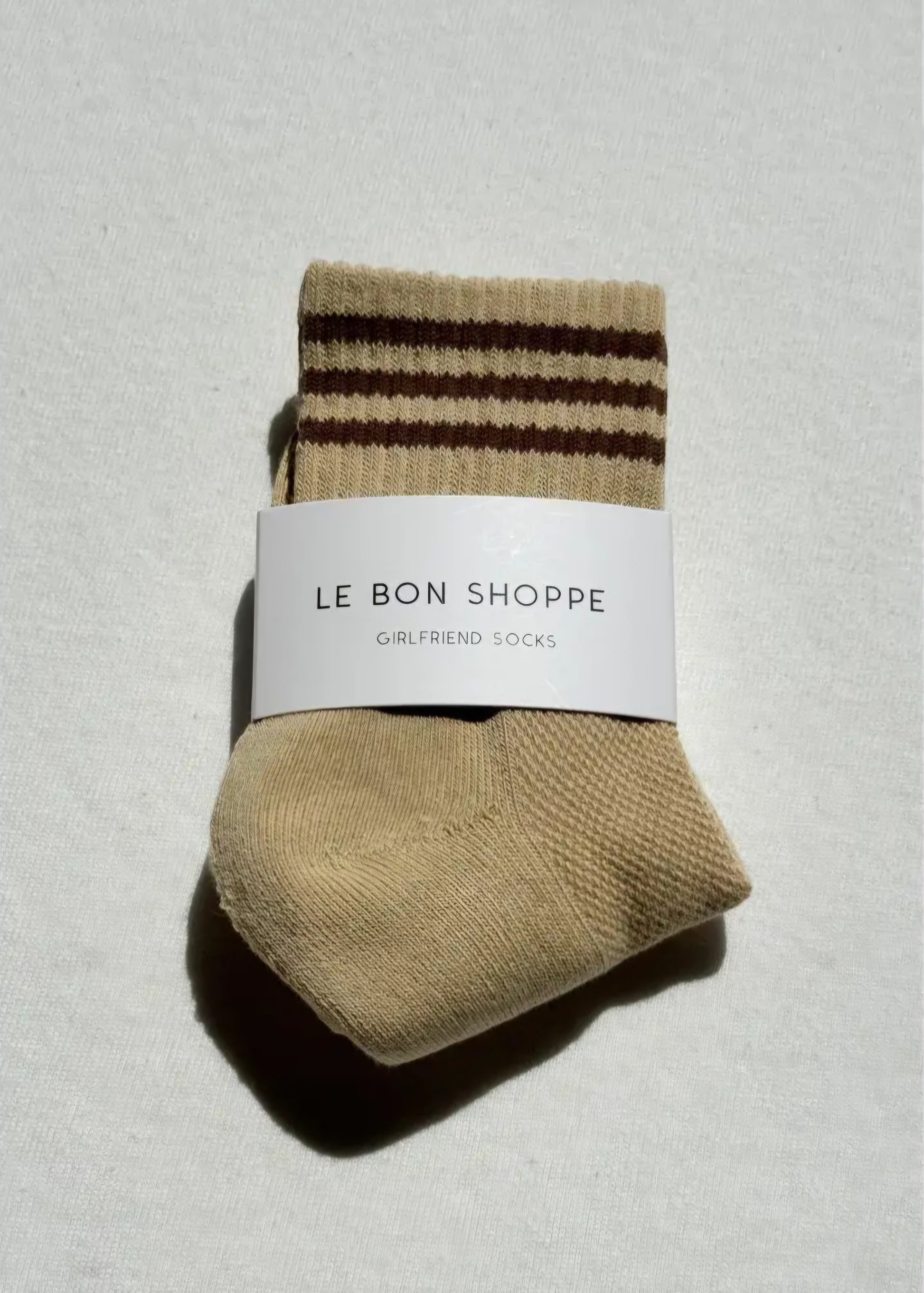 Pair of light yellow socks with brown stripes on a light grey background, featuring 'Le Bon Shoppe' label.