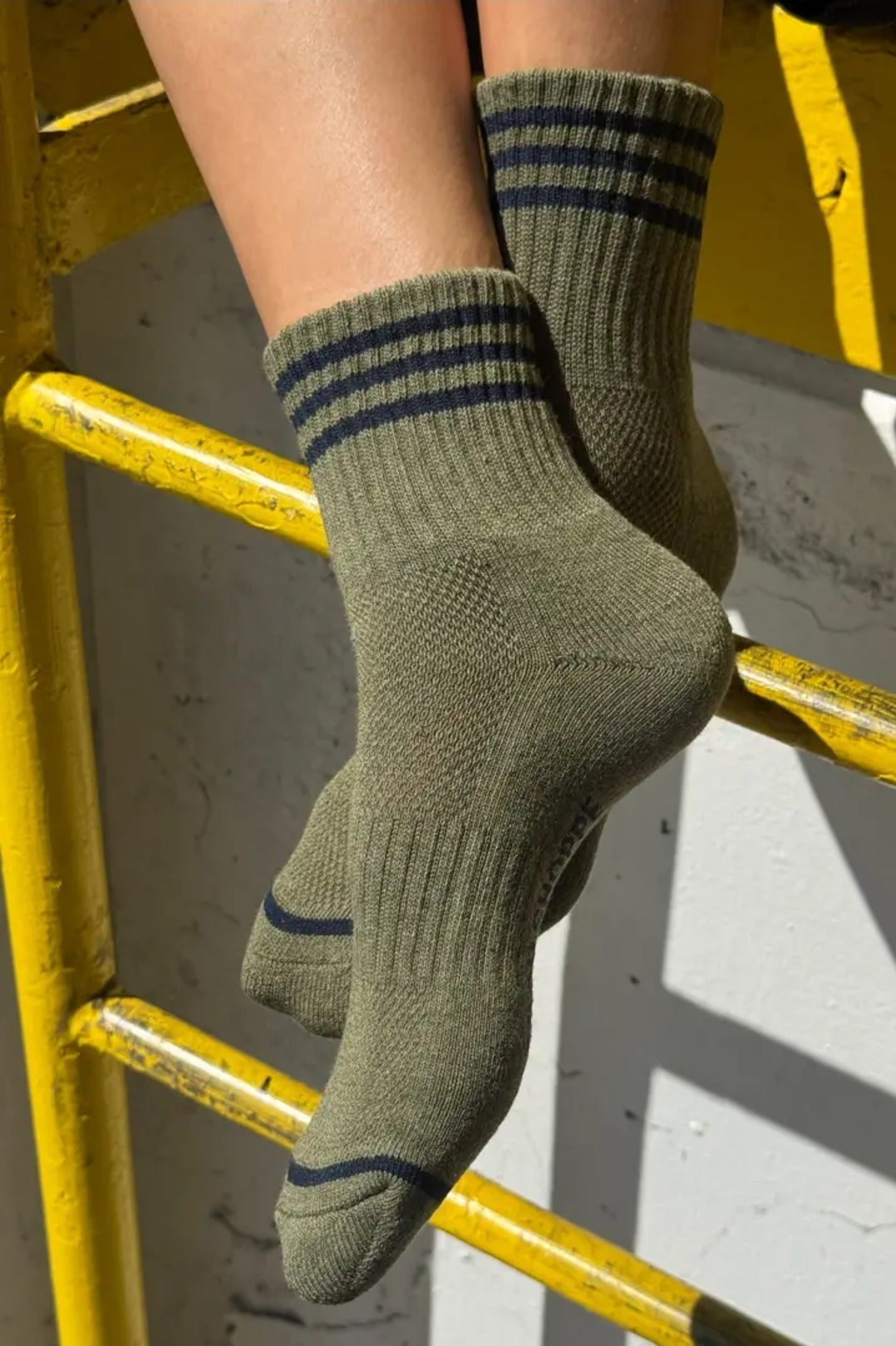 Green socks with blue stripes worn by a person on a yellow metal staircase.