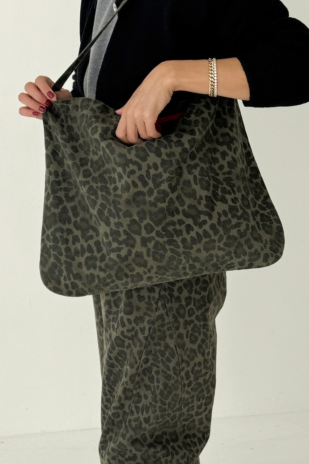 Le Bon Shoppe Happy Carry Bag in fern leopard canvas held by hand, worn with matching trousers.