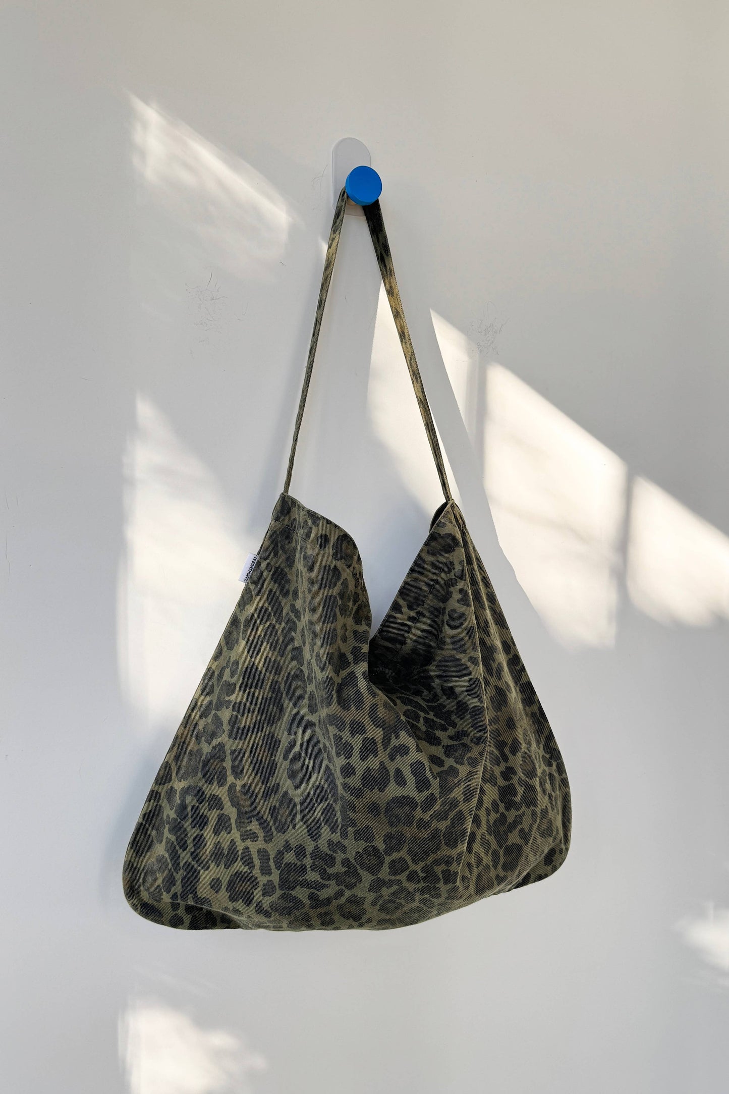 Khaki coloured leopard print bag hanging on a white wall with a blue hook.