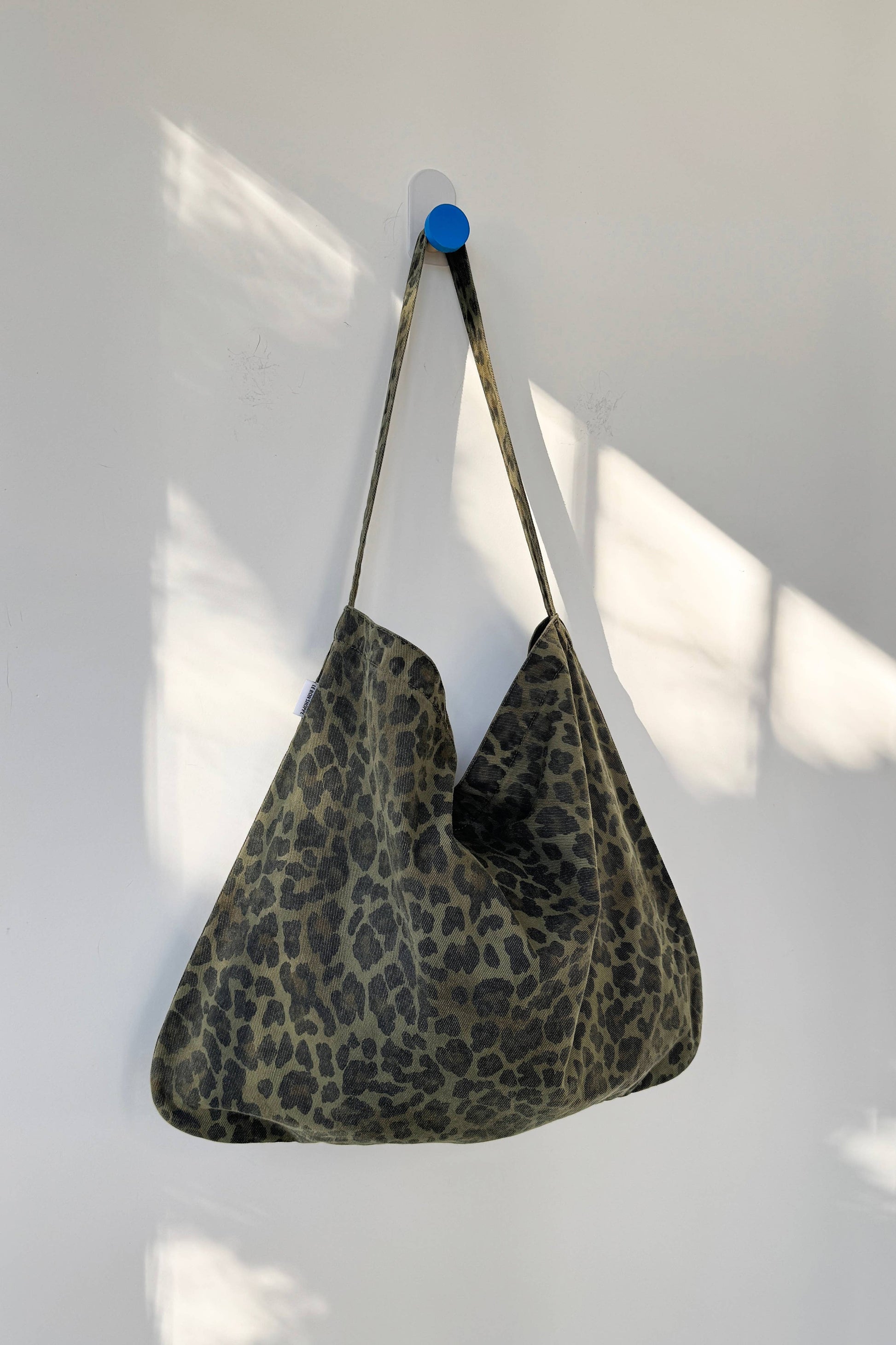 Khaki coloured leopard print bag hanging on a white wall with a blue hook.