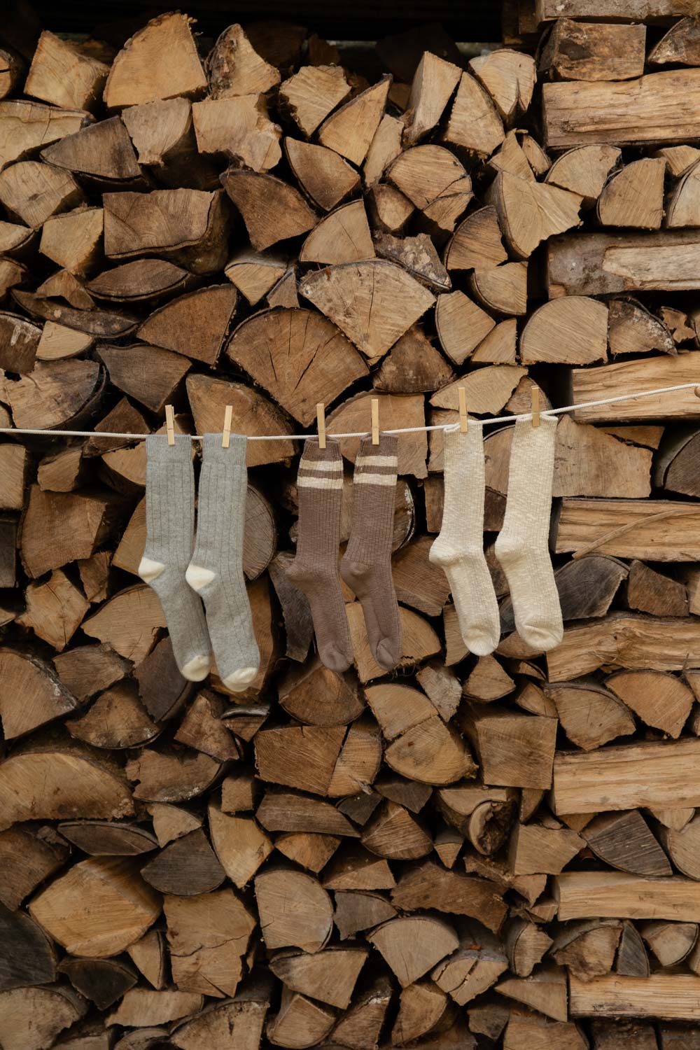 Le Bon Shoppe Classic Cashmere Socks and Cottage Socks in Varsity Stripe and Oatmeal pegged on a line in front of logs