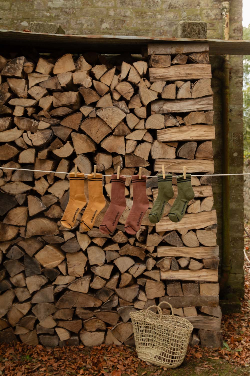 Le Bon Shoppe Boyfriend Socks in Biscotti and Clay and Girlfriend Socks in Sage on a line along a log store
