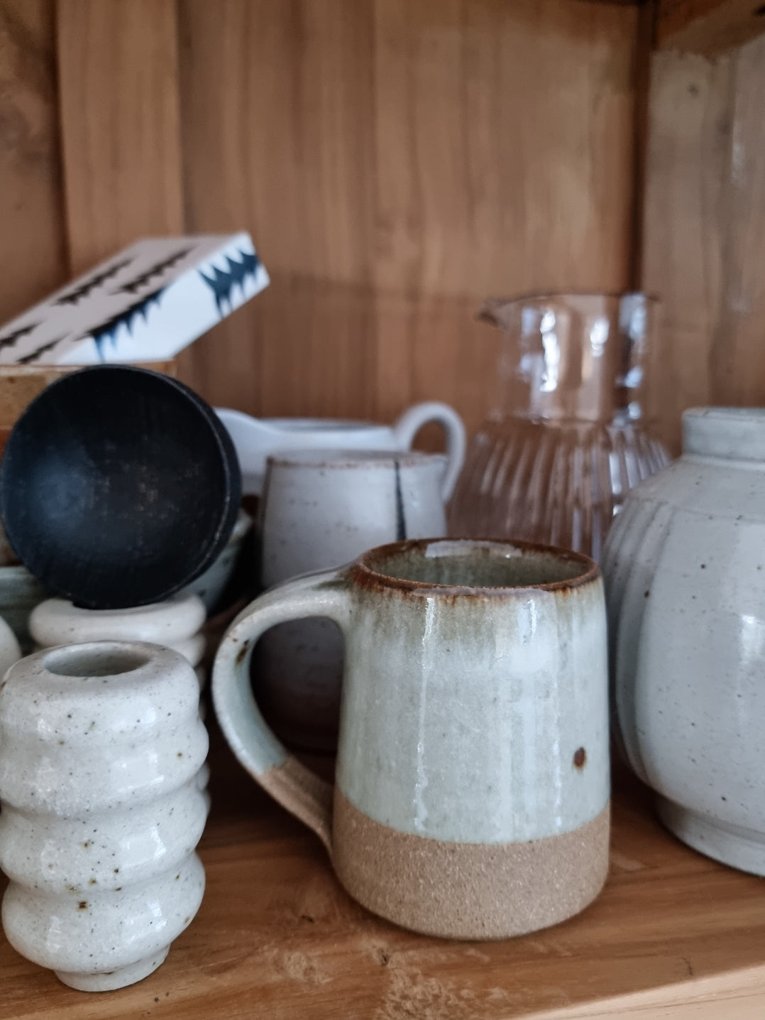 A collection of ceramic pottery including a Leach Pottery dolomite espresso mug displayed on a wooden shelf.